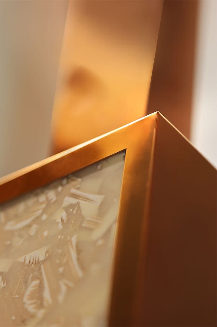 Primer plano de un elemento de escenografía para escaparate: un marco en un cálido tono metálico rodea un panel de textura marcada. El detalle muestra la combinación de materiales, el acabado de los bordes y la precisión de la estructura expositiva.