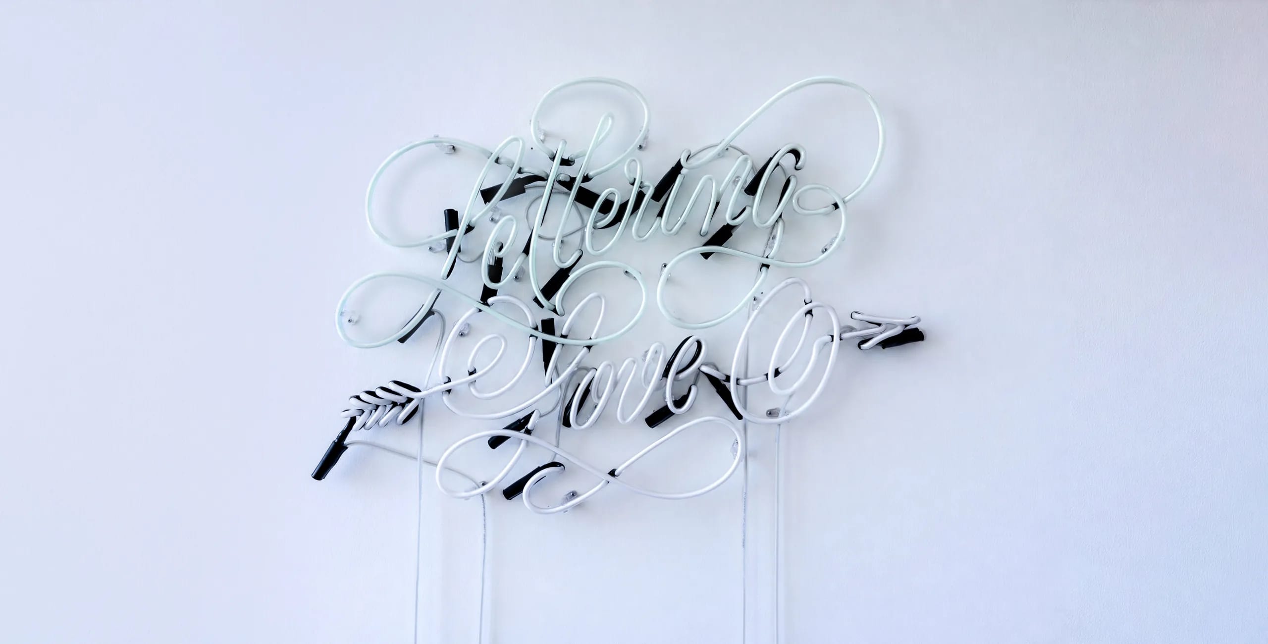 Neon in vetro «Lettering Love» turchese e rosa su una parete chiara